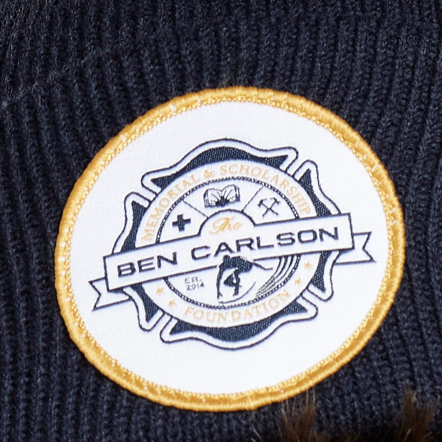 Headshot of a young man wearing a navy blue beanie with a white circular patch on the front.