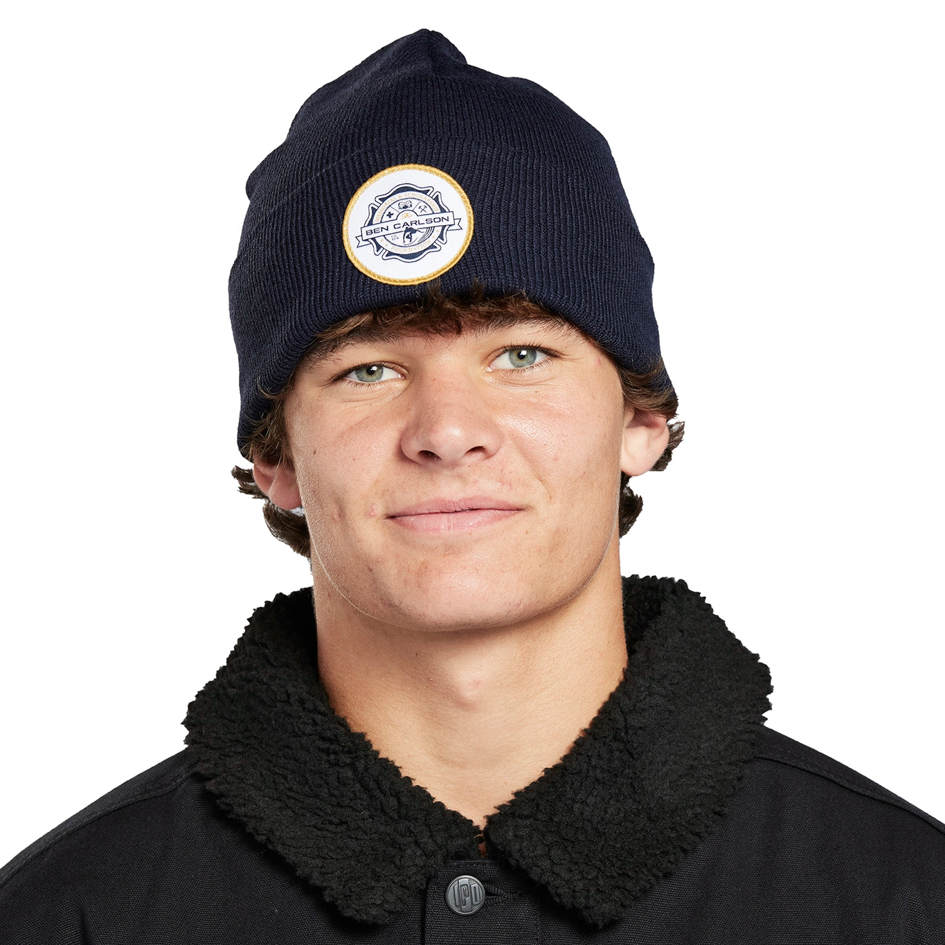 Headshot of a young man wearing a navy blue beanie with a white circular patch on the front.