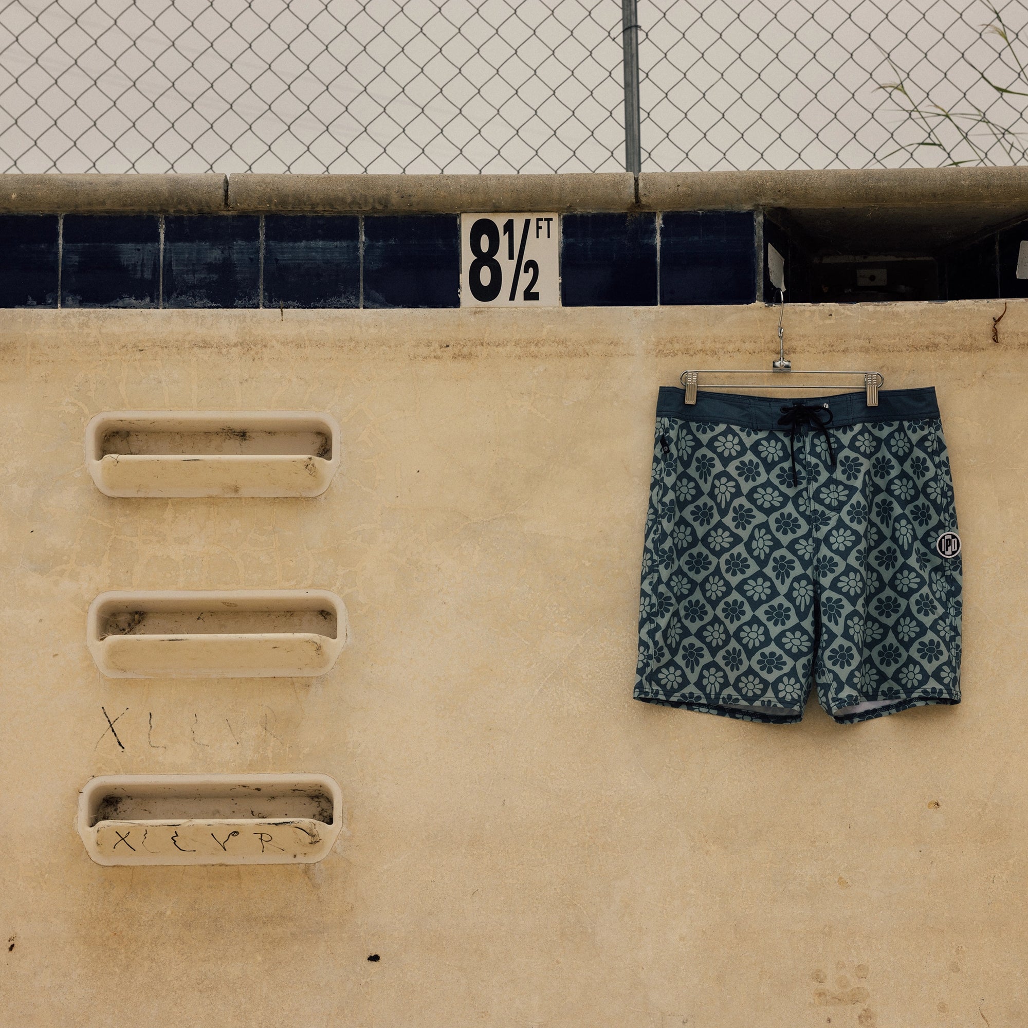 IPD flower print board shorts in blue laid on rocky surface."