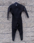Back side of mens wetsuit hanging on wall. Full body with I P D circle logo at the base of neck.