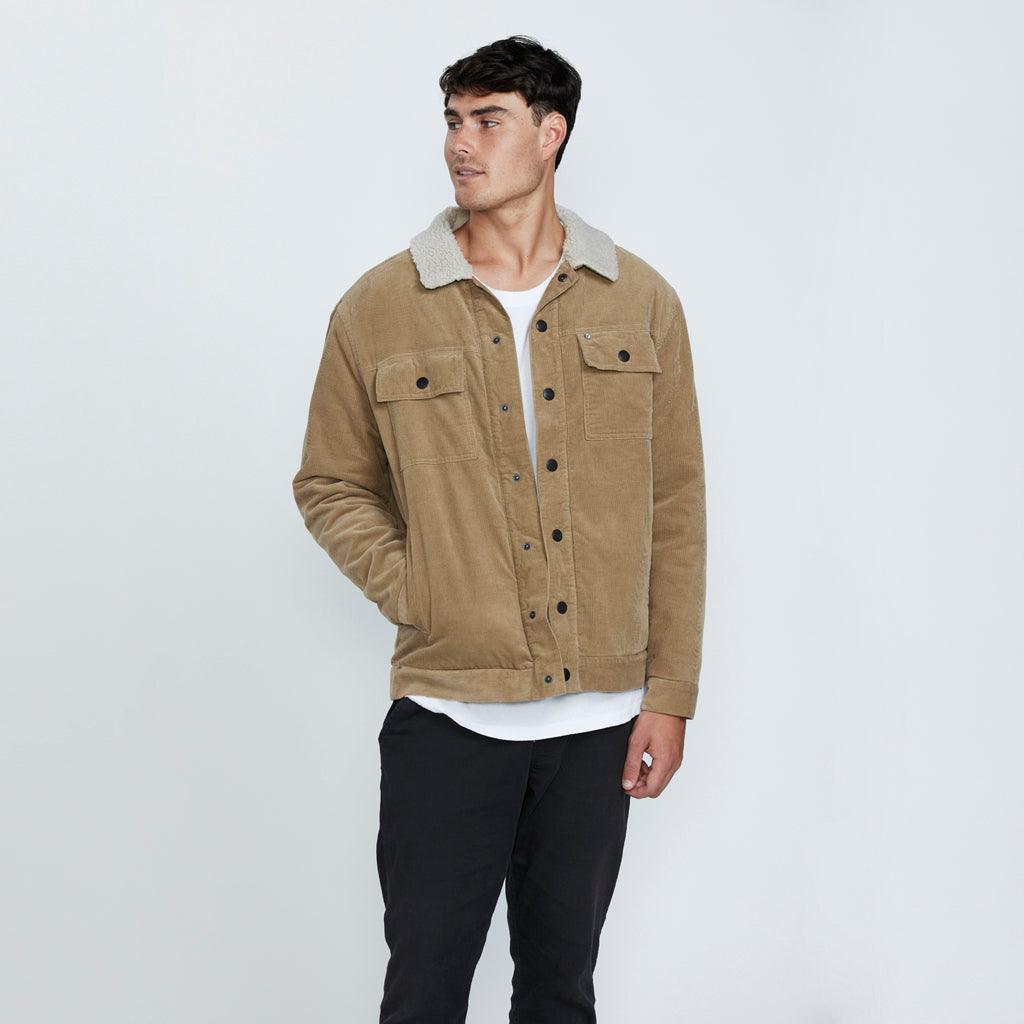 The front view of a man wearing a brown corduroy jacket with his right hand in the right pocket at the waist.