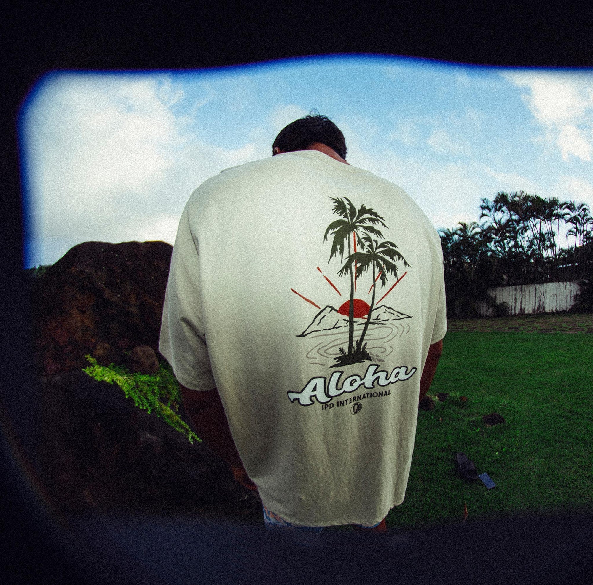 Man wearing white haze short sleeve tee with large Hawaiian themed print and word Aloha on the back.