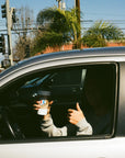 camo - man holds tumbler with logo facing forward and a thumbs up from out car window 