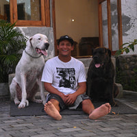 aurelio sitting in front of his house in between his two dogs with a big smile on his face
