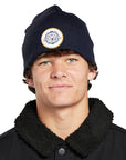 Headshot of a young man wearing a navy blue beanie with a white circular patch on the front.