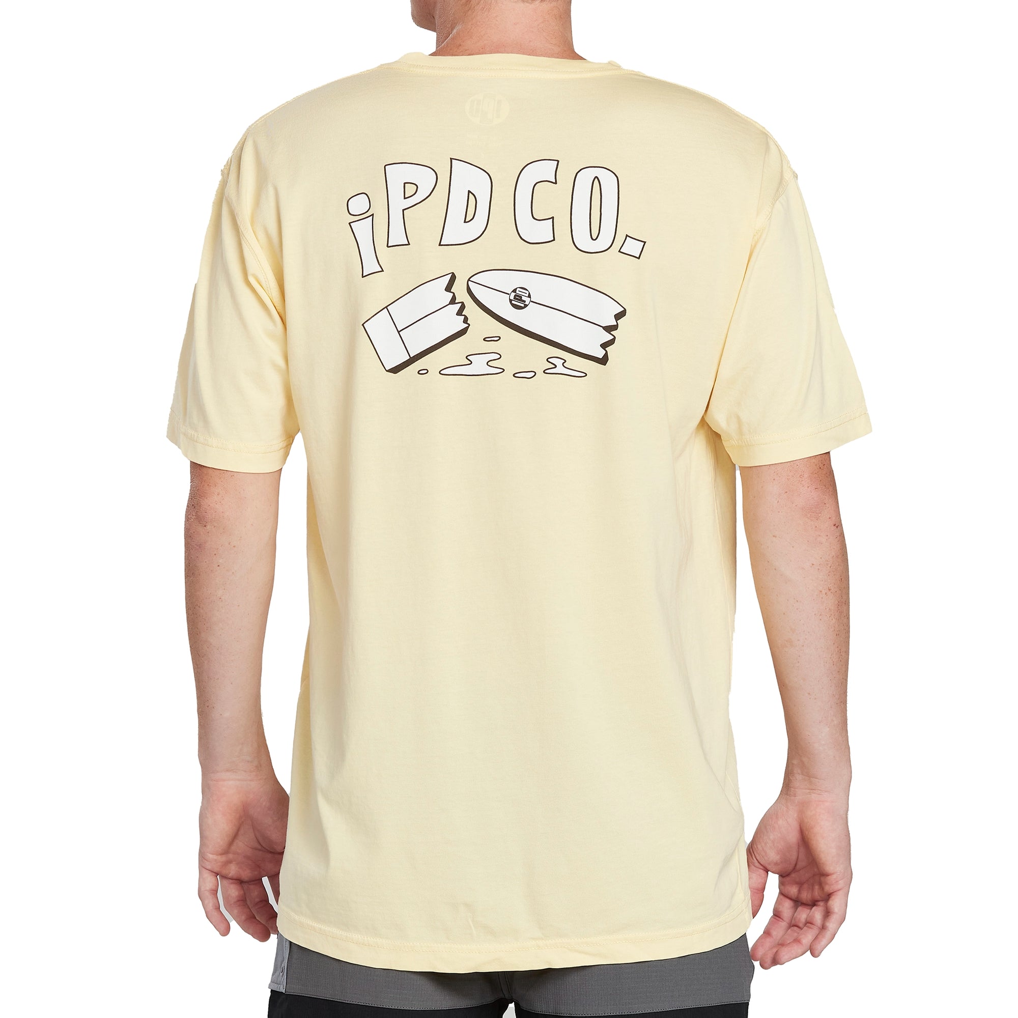Back of a lemonade yellow short sleeve tee with a large print of a cartoon surfboard broken in half. Above the broken surfboard are the letters I P D C O period in a cartoonish font.