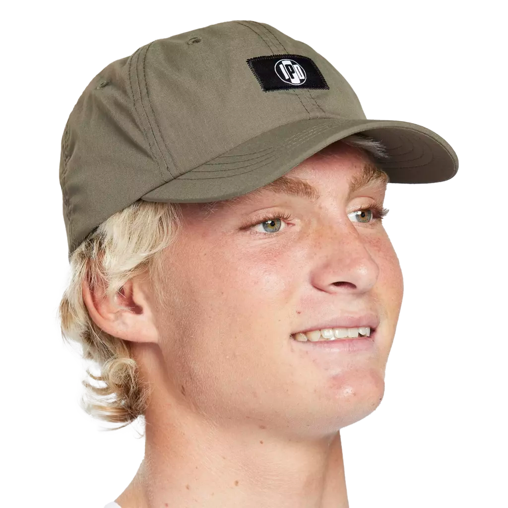 Front side headshot of a young man wearing an olive green hat with a small black rectangular patch on the front. In the middle of the patch is the I P D logo.