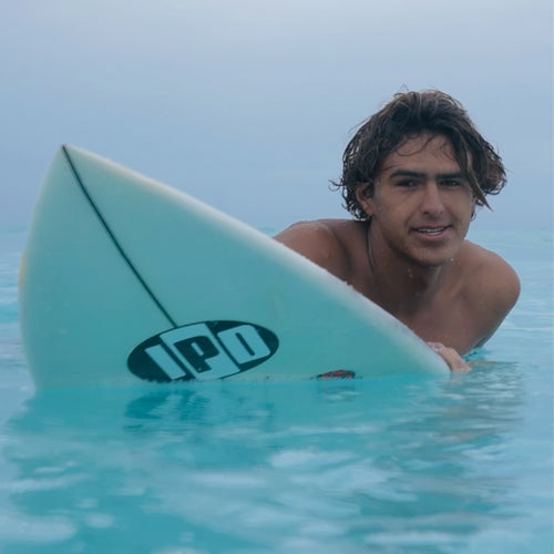 dante in the water looking over his surfboard with a satisfied grin on his face