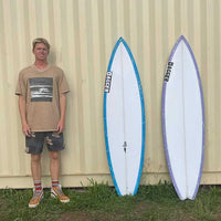 justin casually posing next to two surfboards, all standing next to each other