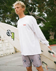 A surfer holds his surfboard while wearing gray moonstone boardshorts with a floral pattern.