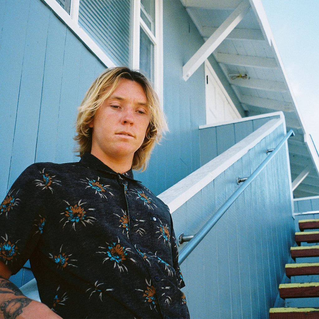 A man wearing a black button up short sleeve shirt with a floral pattern.