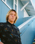 A man wearing a black button up short sleeve shirt with a floral pattern.