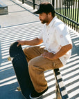 A skater sits on a rail while wearing a white haze short sleeve button up shirt with a floral pattern.