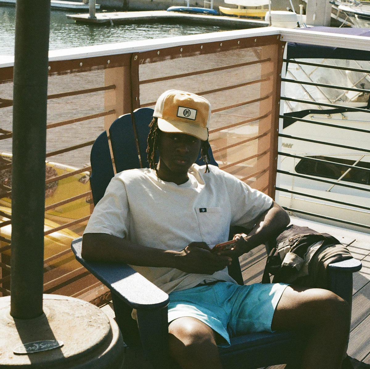 haze - surfer lounges in chair along the water while wearing the mens foundation pocket tee in haze showing front pocket on left chest 