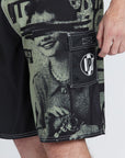 left side view of the mens faceplant Y2k fit 22" boardshort in black showing large graphic on left leg of woman surrounded by IPD logos and pocket with cover and circular IPD logo on it