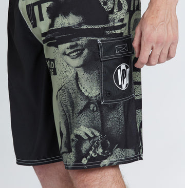 left side view of the mens faceplant Y2k fit 22" boardshort in black showing large graphic on left leg of woman surrounded by IPD logos and pocket with cover and circular IPD logo on it