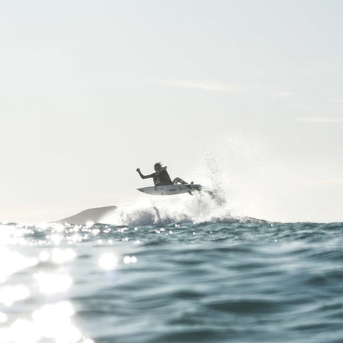 jack airing off a wave, staying on his board in midair with nothing but the sky and a distant mountain behind him