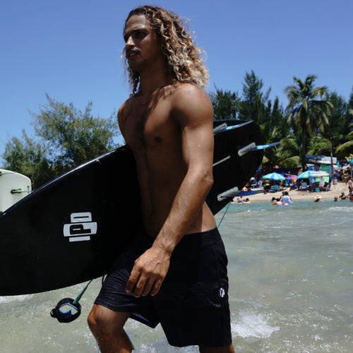 jorgito carrying his surfboard in the water on a crowded beach