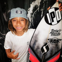 kingston standing next to his surfboard looking stoked and throwing up a shaka sign