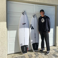 pierce posing in front of his garage rocking an ipd tee with two surfboards by his side