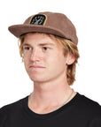 A young man wearing a Paradise brown hat, front view, clearly showing the logo and front design of the hat.