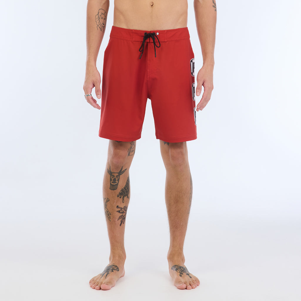 Front view of solid red boardshorts with a black elastic tie on the waistaband.