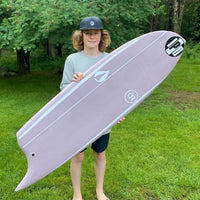 michael standing outside in the grass showing off an asymmetrical surfboard looking stoked