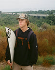 Surfer holding his surfboard while wearing a black water repellent hooded jacket.