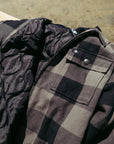 Front chest pocket view of fleece hooded olive flannel jacket with black stripes.