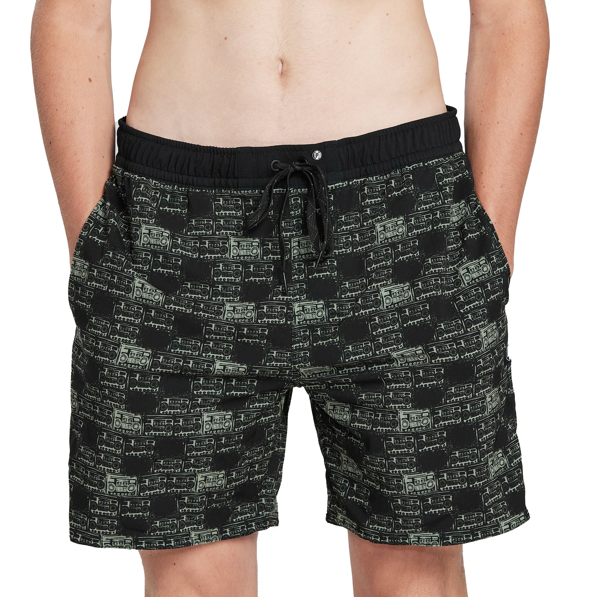 Front of black boardshorts with an alternating pattern of small black and olive green boomboxes covering the boardshorts.