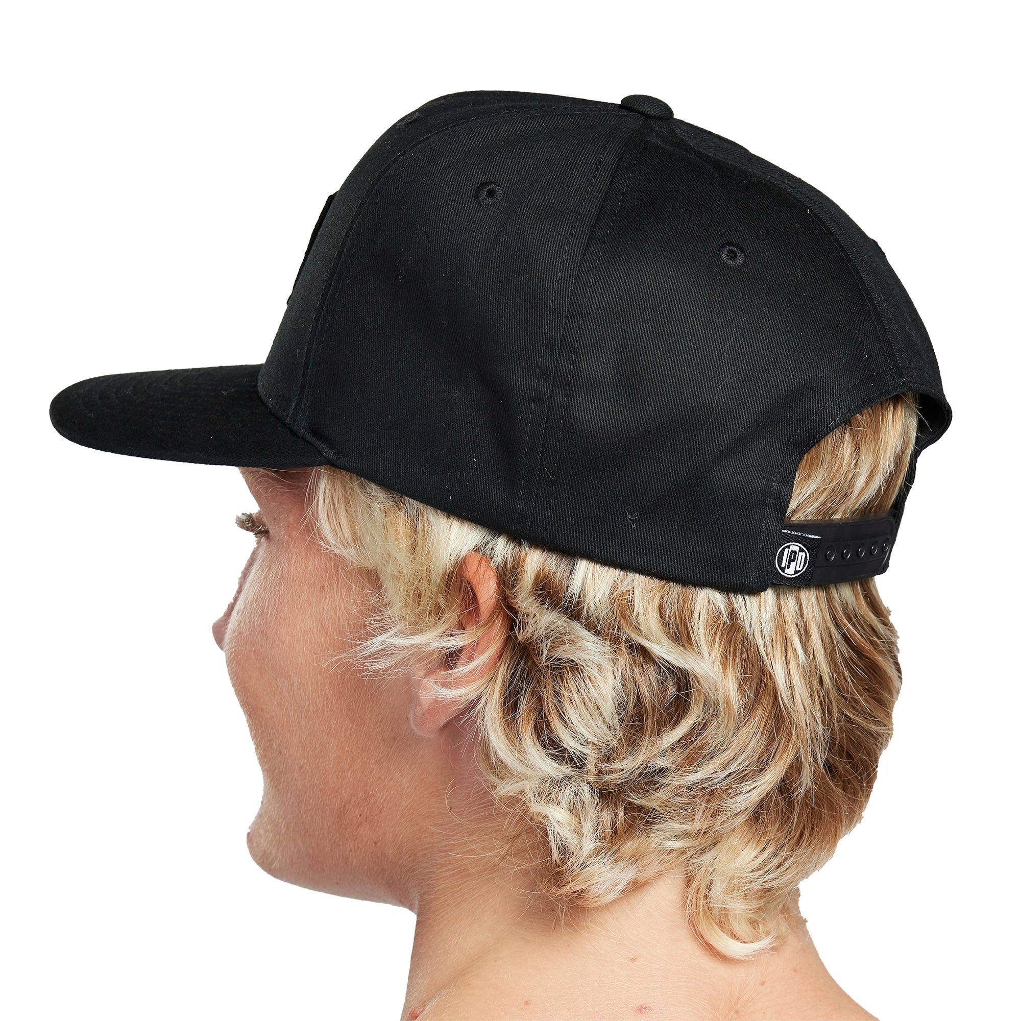 Headshot of a young man wearing a black hat with a white patch on the front. There are two wavy decorative lines running across the middle of the patch. The words I P D Surf Company are above the lines and there's a small I P D logo below the lines with the word Twenty on each side.