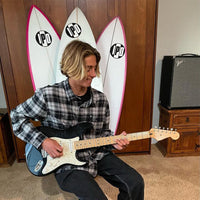 tyler sitting inside playing his electric guitar with three surfboards set up behind him