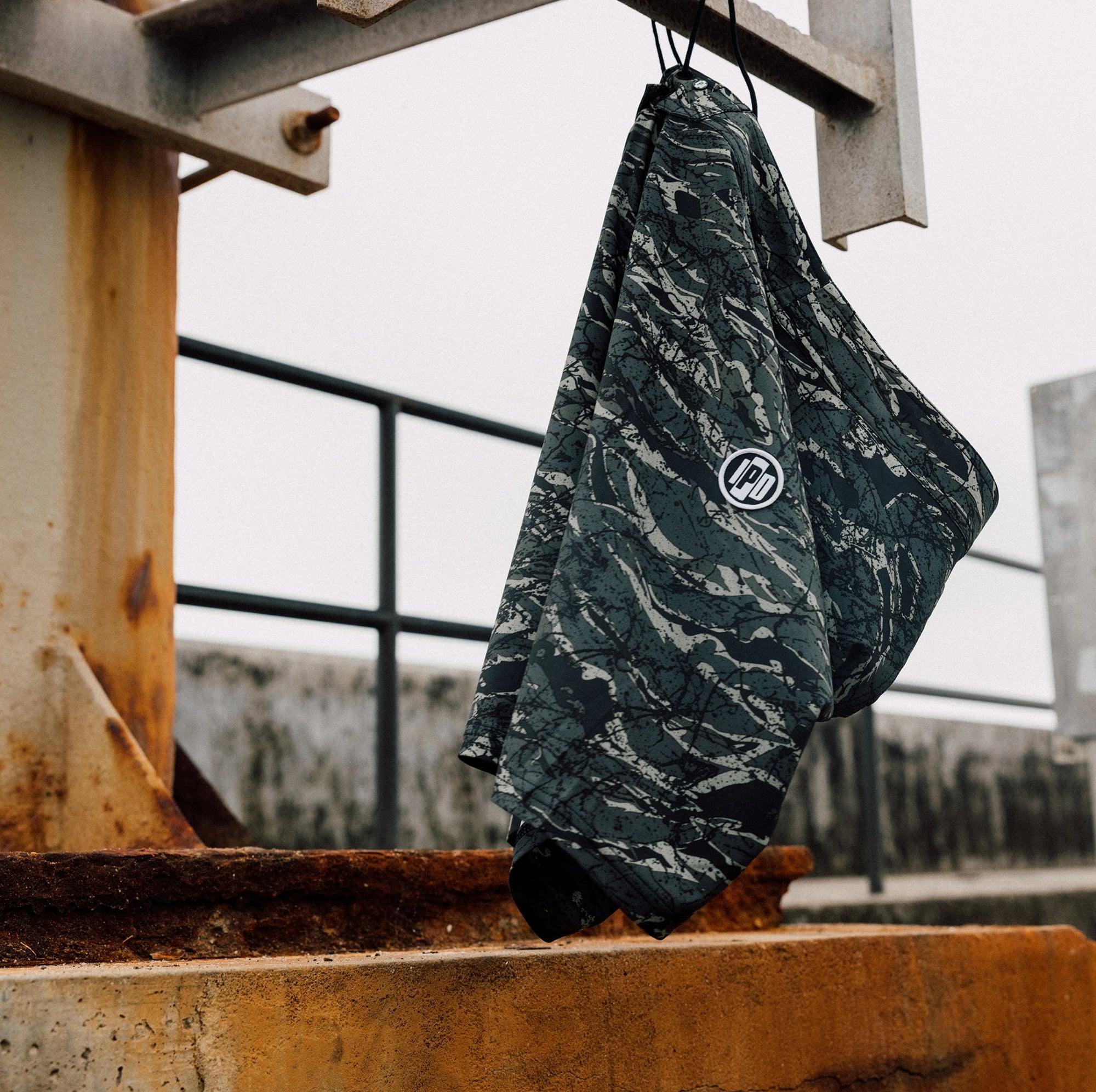 Camouflage board shorts hanging in an industrial setting. Made with 86% recycled polyester and 14% spandex. Features a 20-inch straight hem outseam, zigzag interior stitch waistband, and a signature metal rivet.
