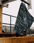 Camouflage board shorts hanging in an industrial setting. Made with 86% recycled polyester and 14% spandex. Features a 20-inch straight hem outseam, zigzag interior stitch waistband, and a signature metal rivet.