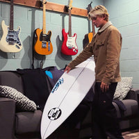 dylan holding his surfboard over a couch that sits under a nice guitar collection hanging on the wall