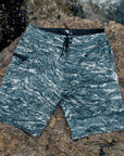 Camouflage board shorts laid out on rocks by the ocean. Made from 86% recycled polyester and 14% spandex. Features a 20-inch straight hem outseam and stretch mesh pocket bag.