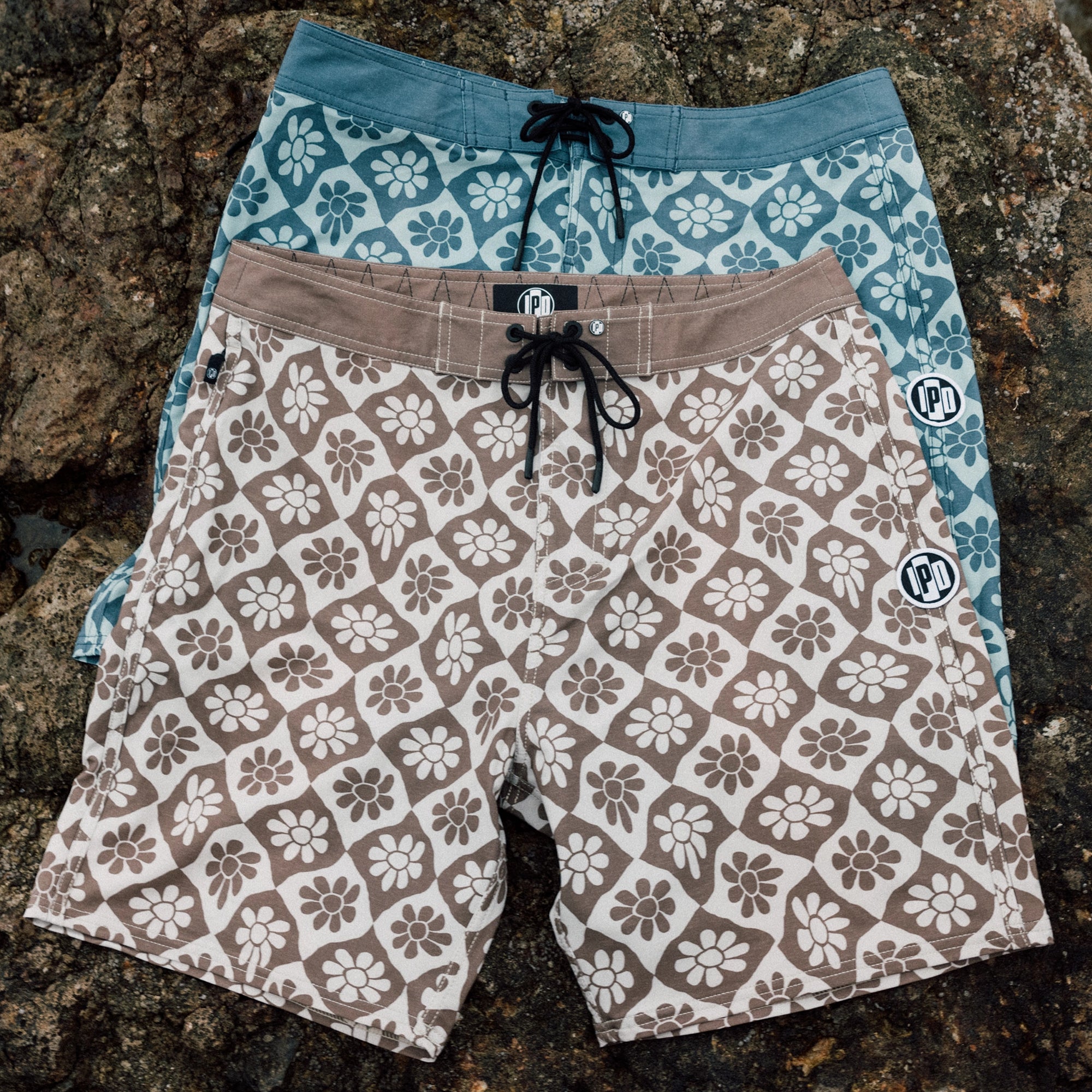Blue and brown IPD flower print board shorts layered on rocks.