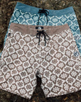 Blue and brown IPD flower print board shorts layered on rocks.