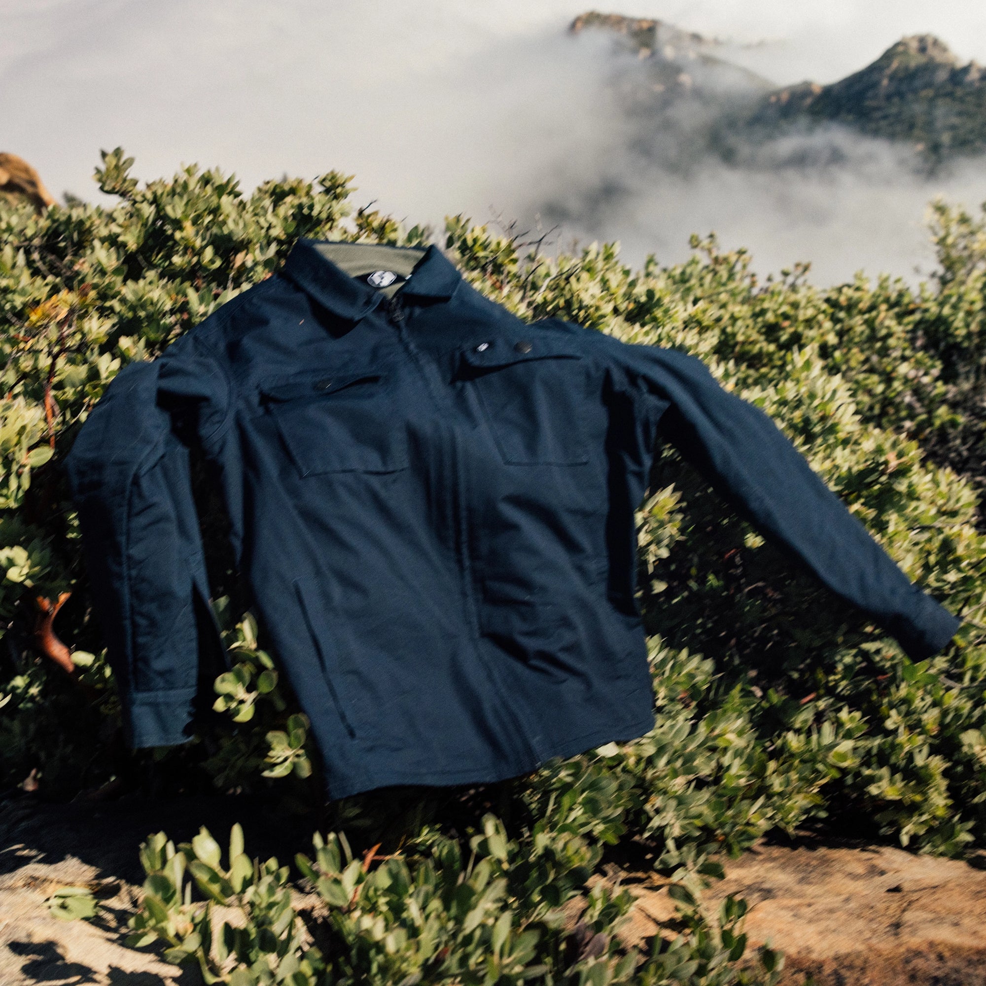 IPD  jacket displayed outdoors on a bush with a scenic mountain background