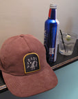 IPD Paradise corduroy hat displayed on a shelf with a drink and beer can in the background