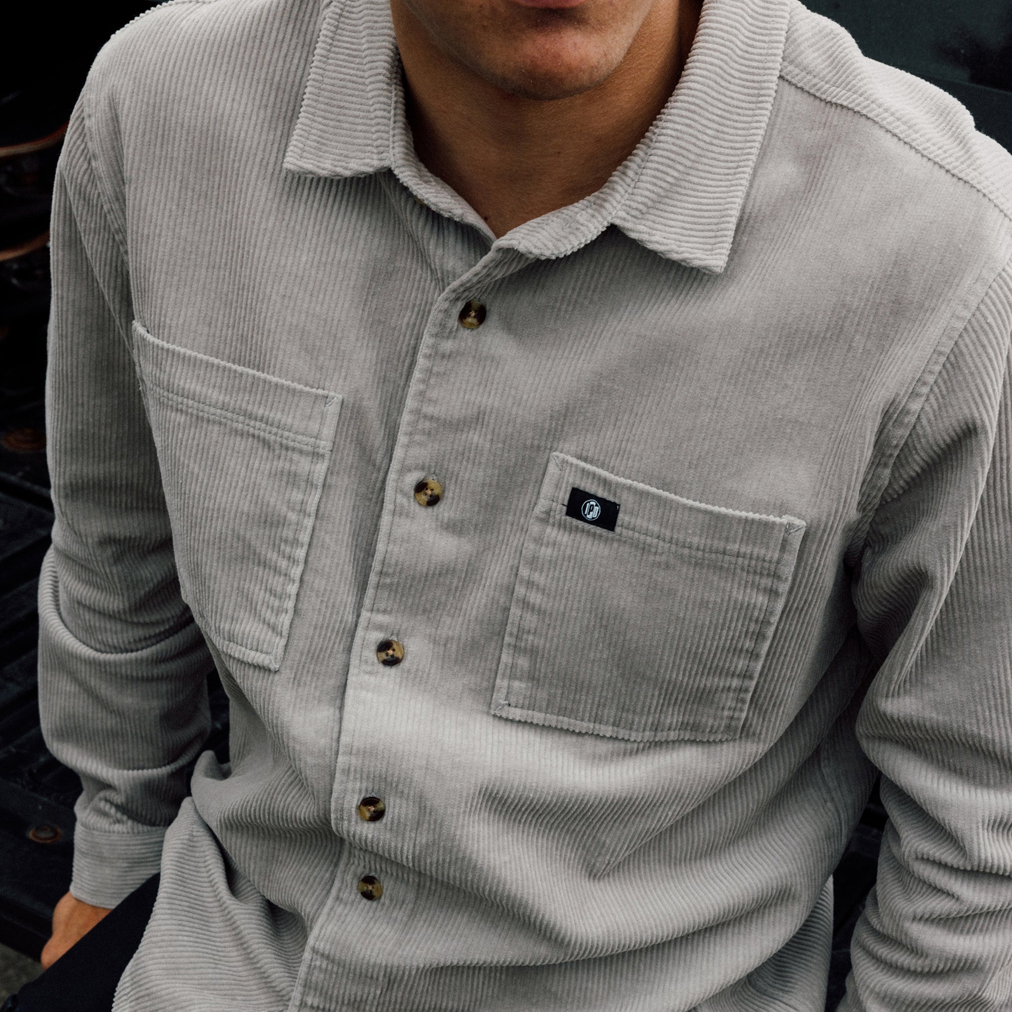 Man wearing the IPD Pierside corduroy shirt in haze, seated outdoors.