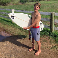 jesse standing in boardies holding his surfboard with a big smile on his face