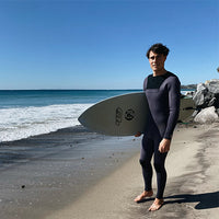 noah standing on the beach with wetsuit on and board in hand ready to surf