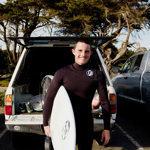 sam looking happy and ready to surf with wetsuit on and board in hand 