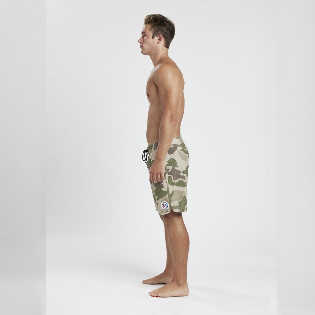 model wearing mens bridgae 83 fit 18&quot; boardshort in camo showing side view with international pro design circular logo surrounding USA on left thigh logo
