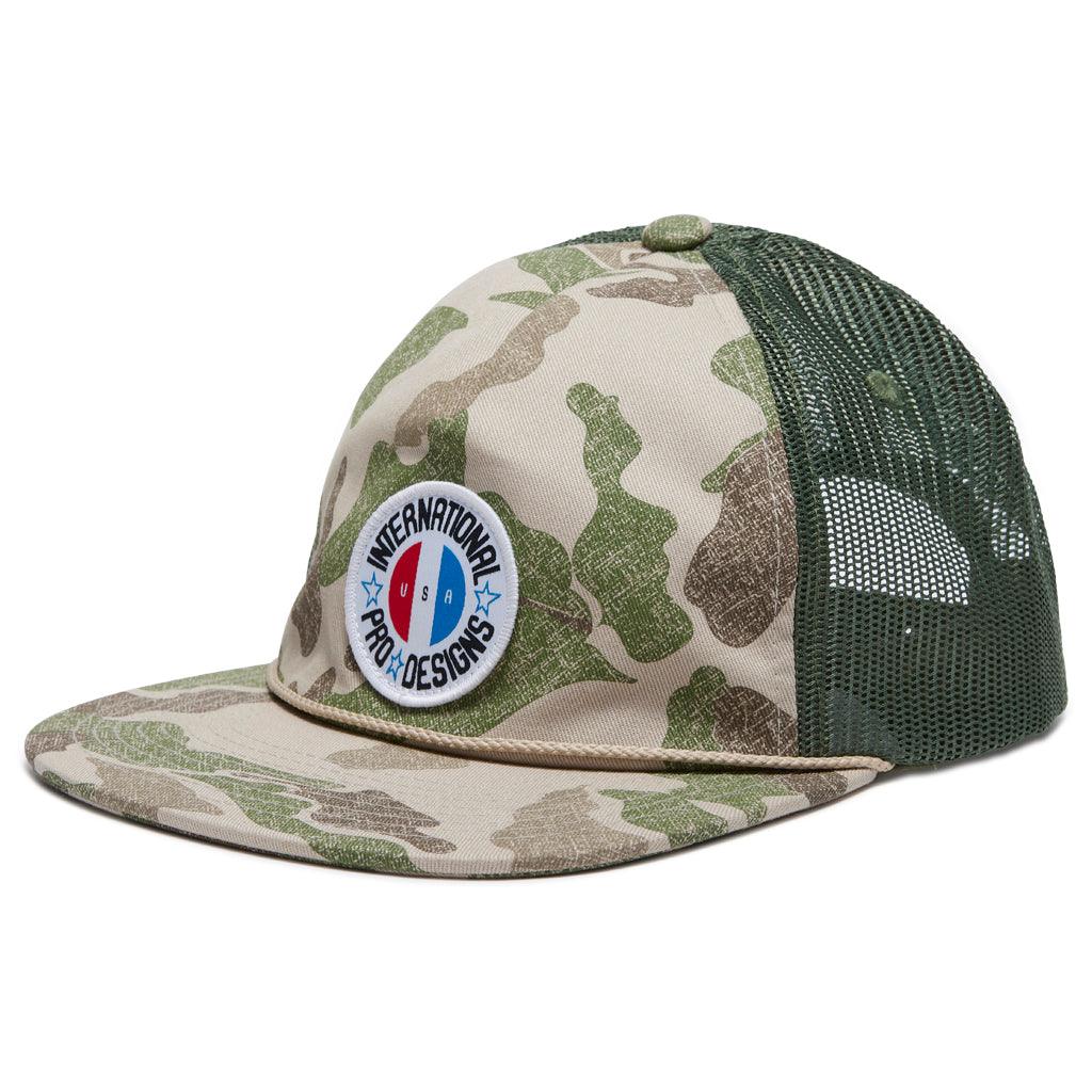 partial side view of the brigade trucker snapback hat showing the camo front and mesh back. Showing the logo patch on front that is internationla pro designs surrounding circular USA logo 