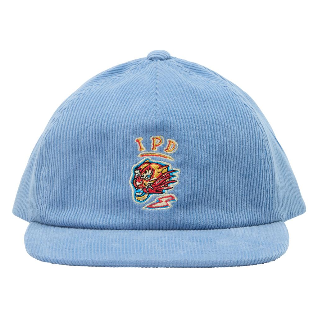 The Tiger Corduroy Hat features a classic light blue corduroy fabric with a strap closure in the same fabric and color. The front features an embroidered tiger head with IPD lettering above it in the colors red, yellow, orange, and blue.