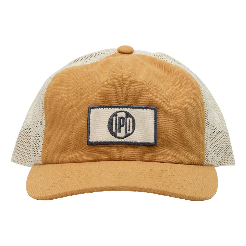 The 1697 Trucker Snapback features a lower profile trucker styling in the color brass with a white mesh back. It features a white and green rectangular front patch with the I P D logo in the center.