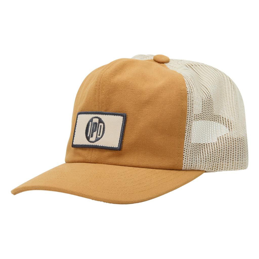 The 1697 Trucker Snapback features a lower profile trucker styling in the color brass with a white mesh back. It features a black and green rectangular front patch.