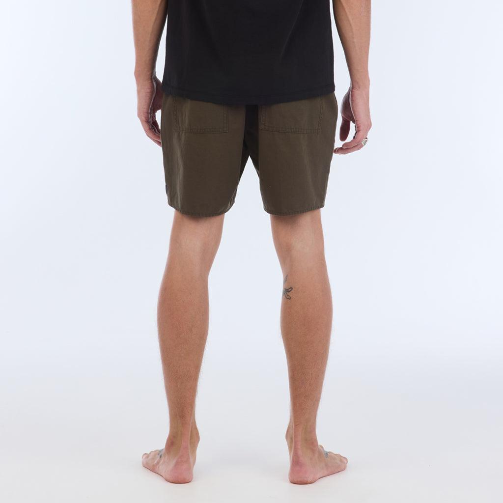 on model with black top. back view:The Foundation Walkshort is a classic walkshort silhouette that comes in at a 17” length. It features a solid olive coloring, and features an elastic waistband and drawcord. The pocketing is two side pockets and two back patch pockets. It features the signature smaller IPD flag label on the lower left leg.